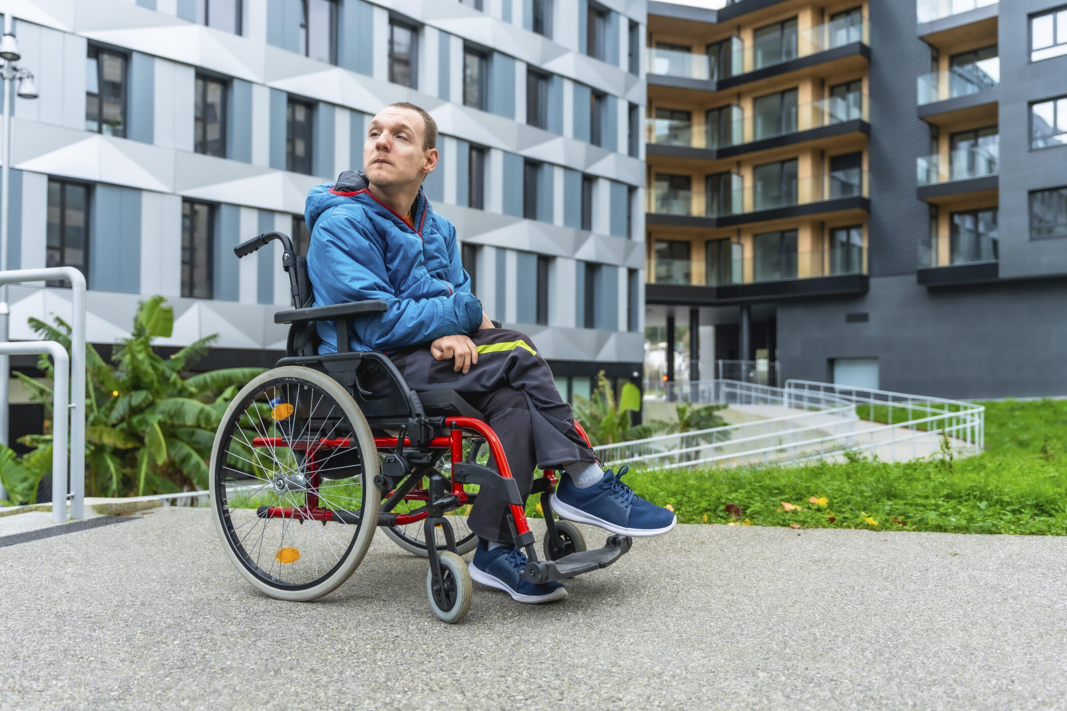 Person im Rollstuhl auf Gehweg vor modernem Gebäude.