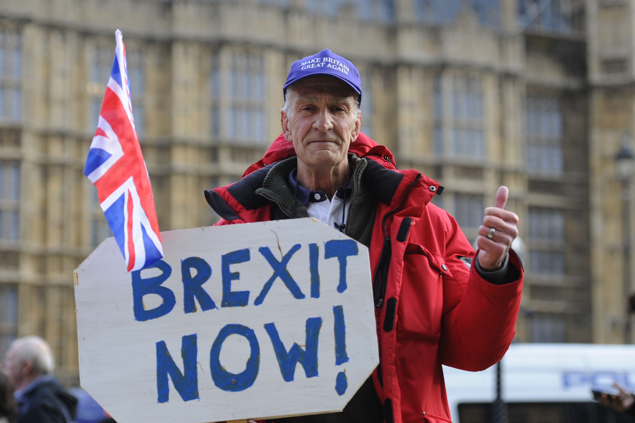 Person mit Brexit-Schild und Union Jack Fahne vor einem Gebäude.