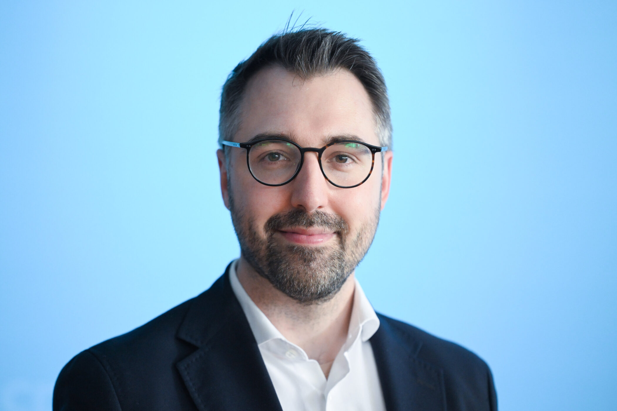 Eine Person mit Brille vor blauem Hintergrund.