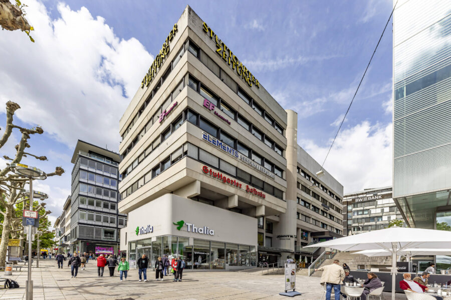 Mehrstöckiges Gebäude mit Geschäften, Menschen gehen vorbei, Straßencafé mit Personen.