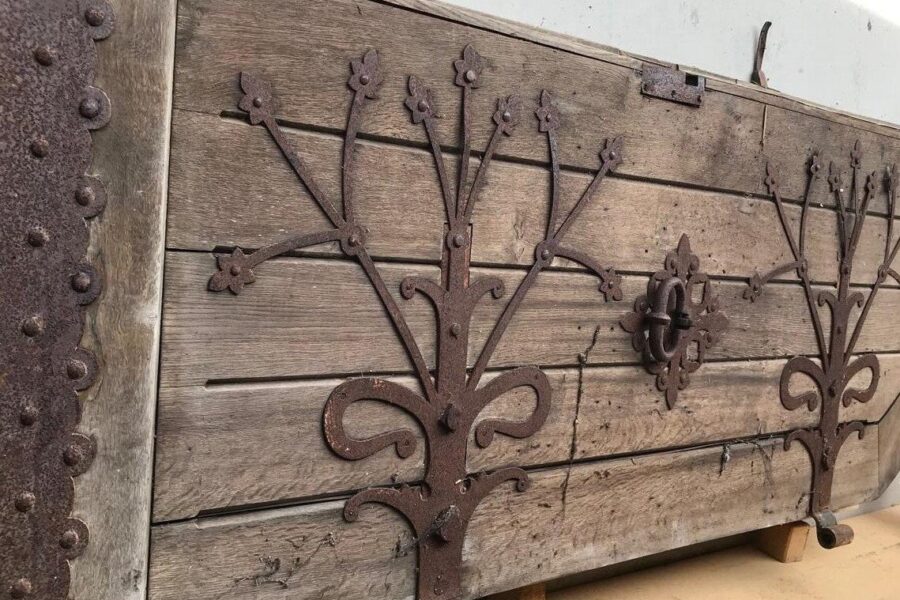 Holztür mit rostigen Metallverzierungen und Beschlägen.
