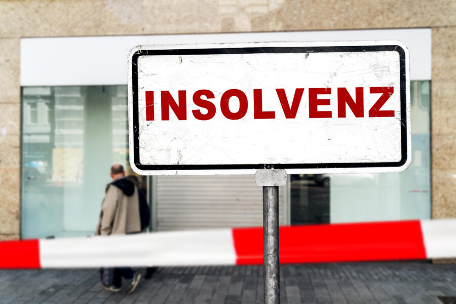 Schild mit der Aufschrift "INSOLVENZ", zwei Personen gehen vorbei.