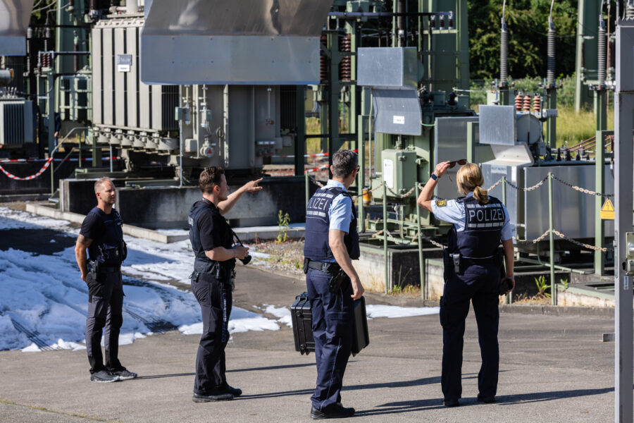 Vier Polizisten in Uniformen bei einem Industriekomplex.