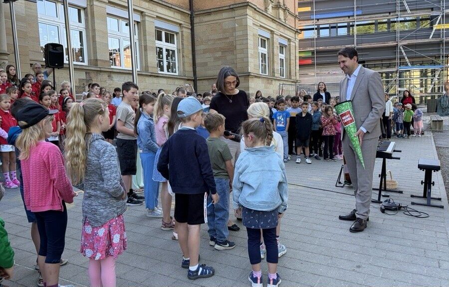 Gruppe Kinder bei einer Schuleröffnung im Freien, Erwachsene mit Schultüte daneben.