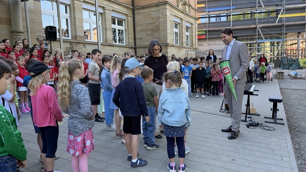 Gruppe Kinder bei einer Schuleröffnung im Freien, Erwachsene mit Schultüte daneben.