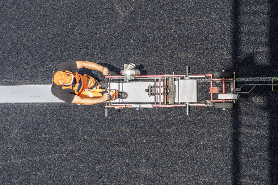 Ein Bauarbeiter in orangefarbener Kleidung arbeitet auf frischem Asphalt.