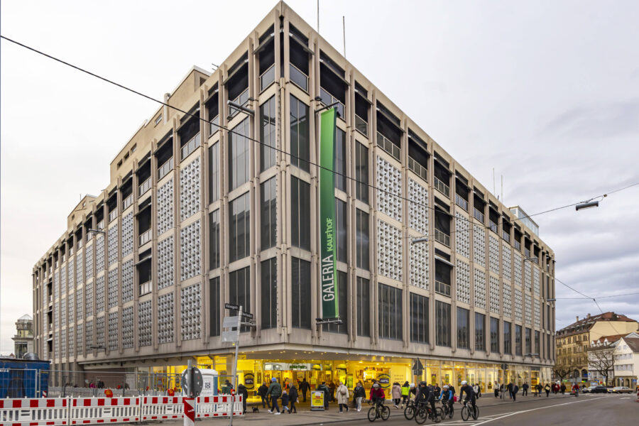 Eckgebäude mit Glasfassade, Menschen und Fahrräder auf der Straße.