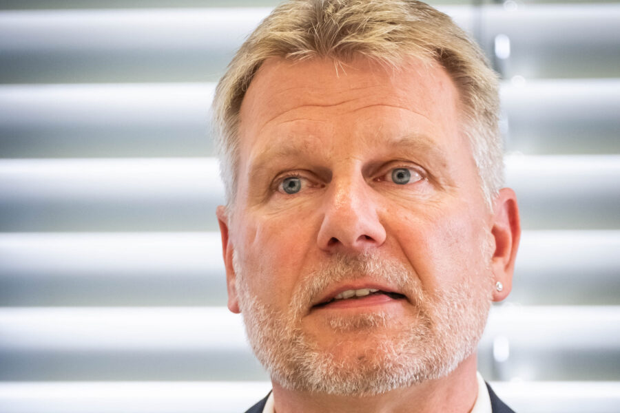 Eine Person mit Bart vor Jalousie im Hintergrund.