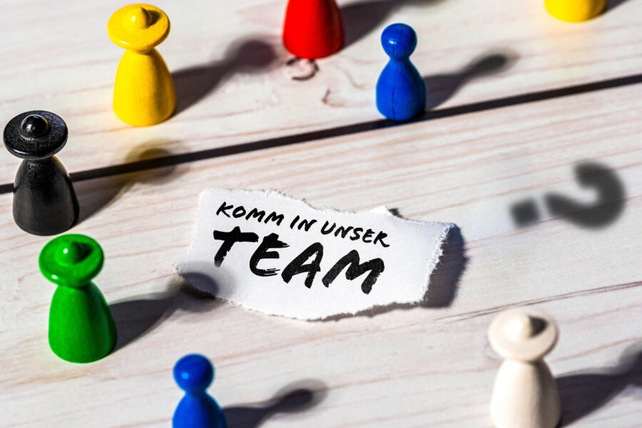 Bunte Spielfiguren auf Holz, Text: "Komm in unser Team".