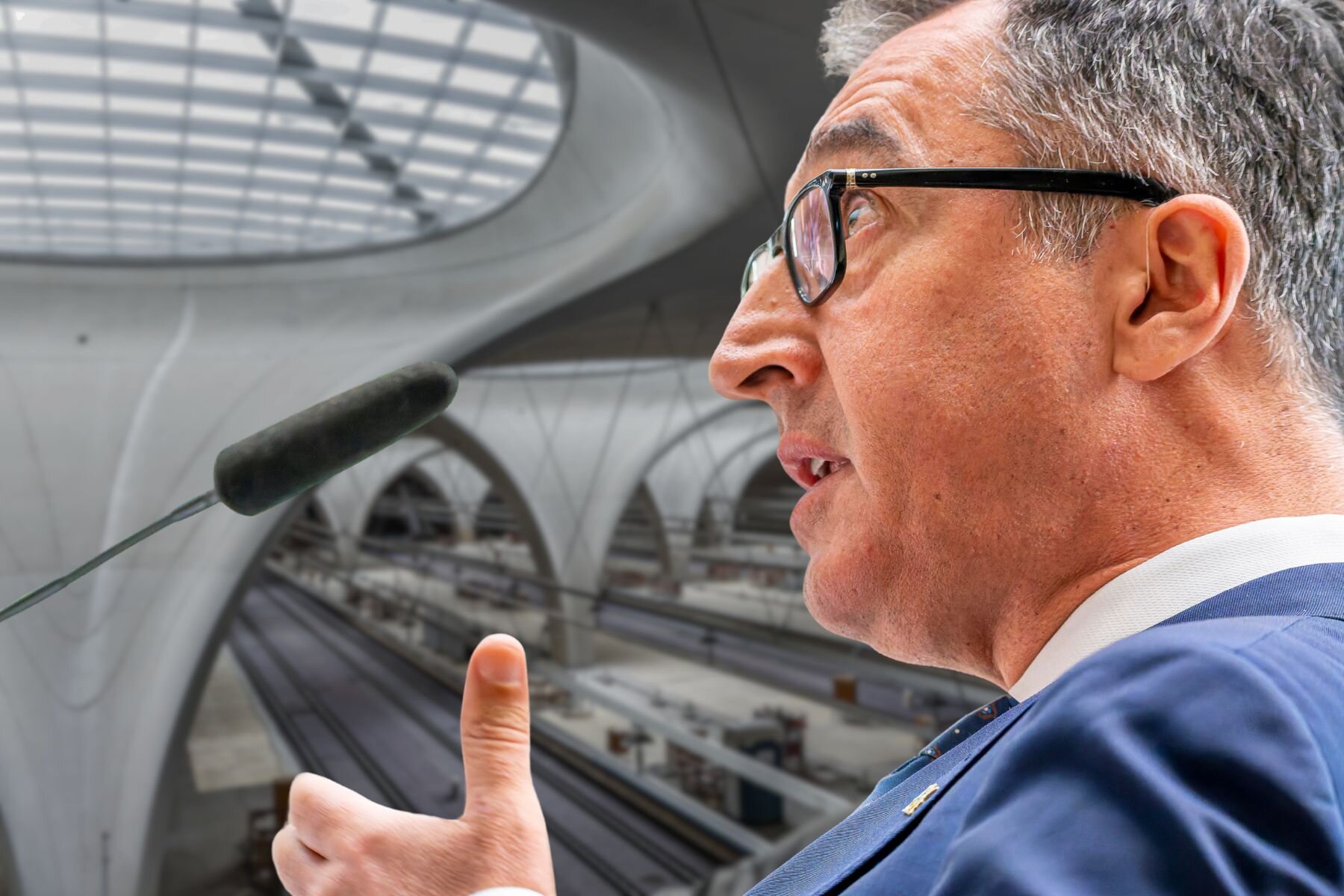 Person am Mikrofon, moderner Bahnhof im Hintergrund.