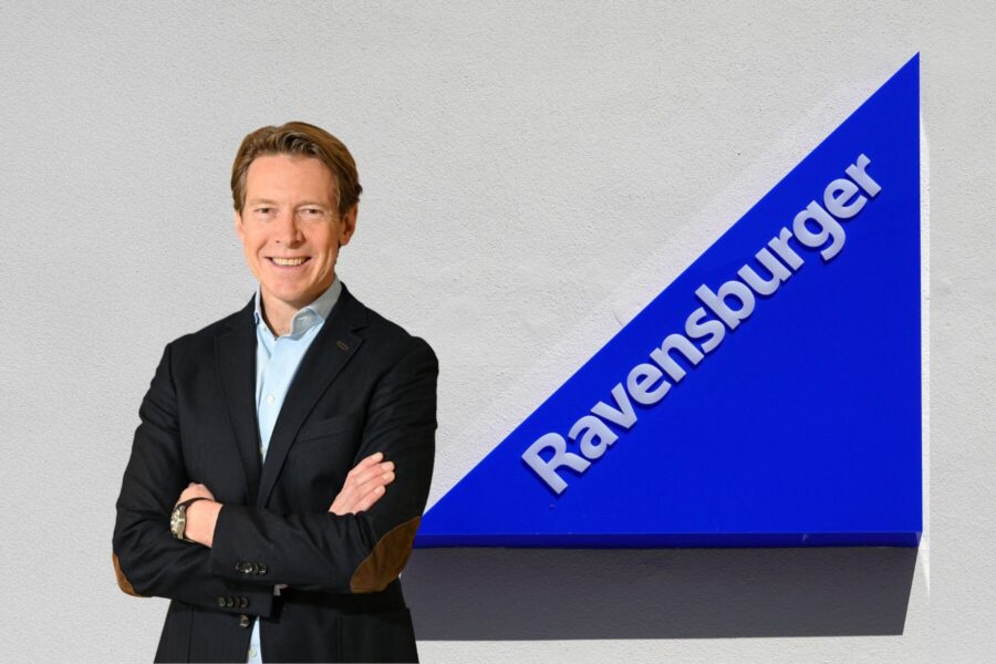Eine Person lächelt, neben einem blauen Schild mit "Ravensburger".