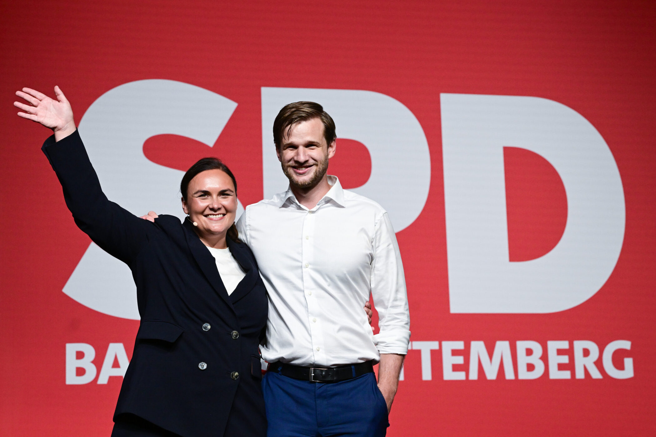 Zwei Personen lächelnd vor rotem Hintergrund mit großem SPD-Logo.
