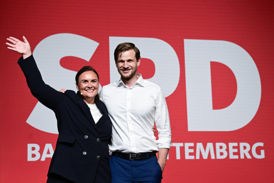 Zwei Personen lächelnd vor rotem Hintergrund mit großem SPD-Logo.