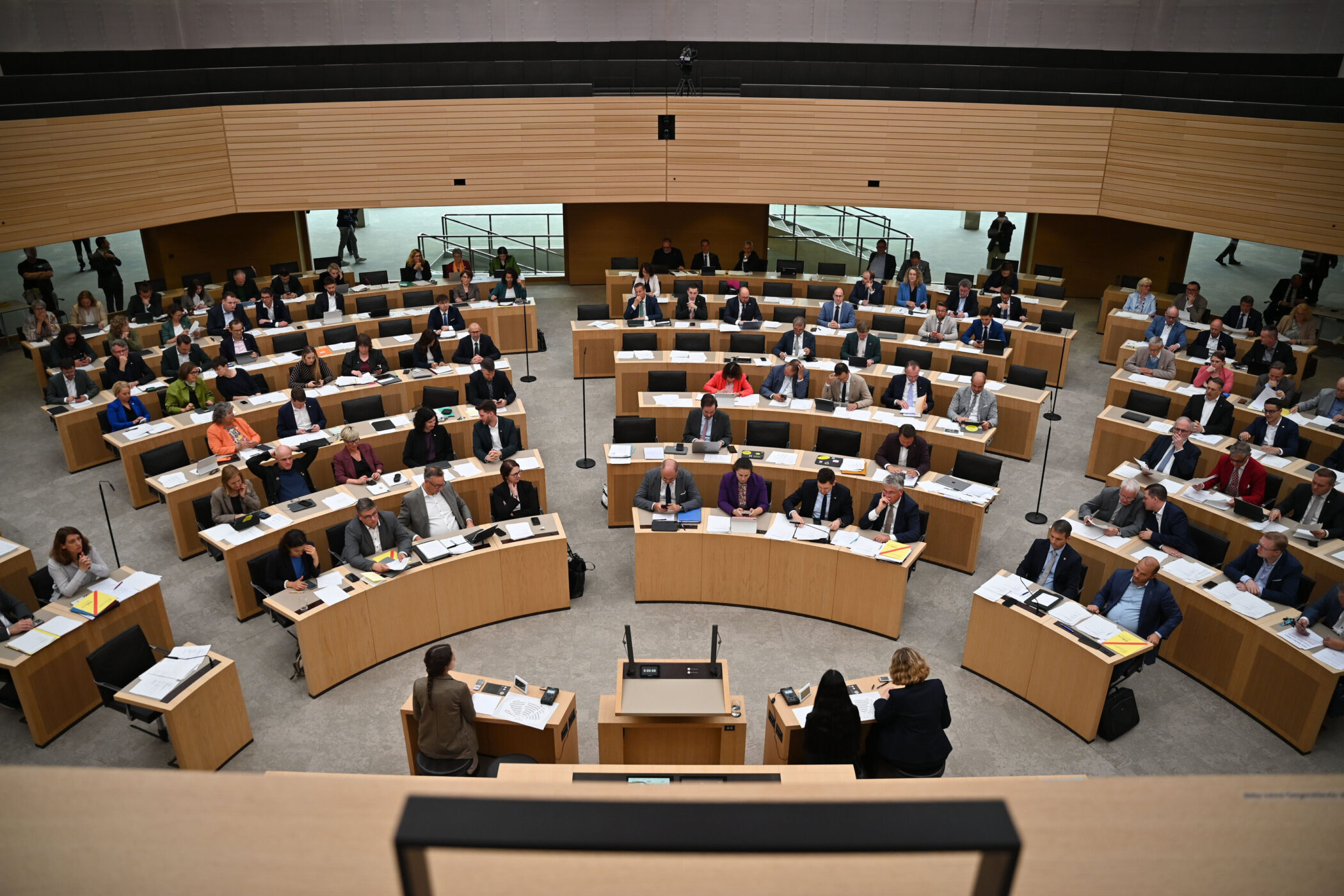 Viele Menschen sitzen an Tischen in einem großen Saal, von oben fotografiert.