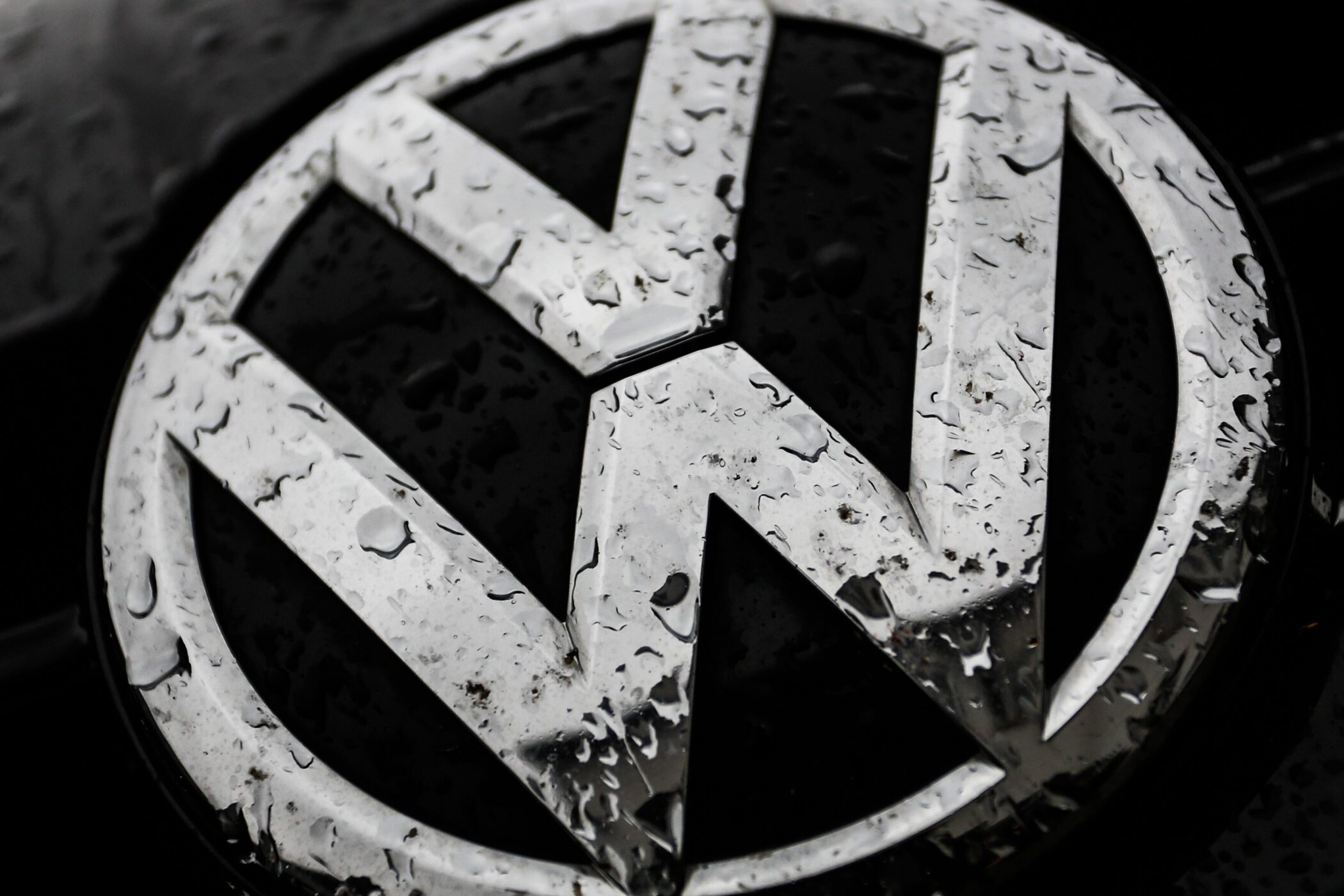 Silbernes VW-Logo mit Wassertropfen bedeckt auf dunklem Hintergrund.