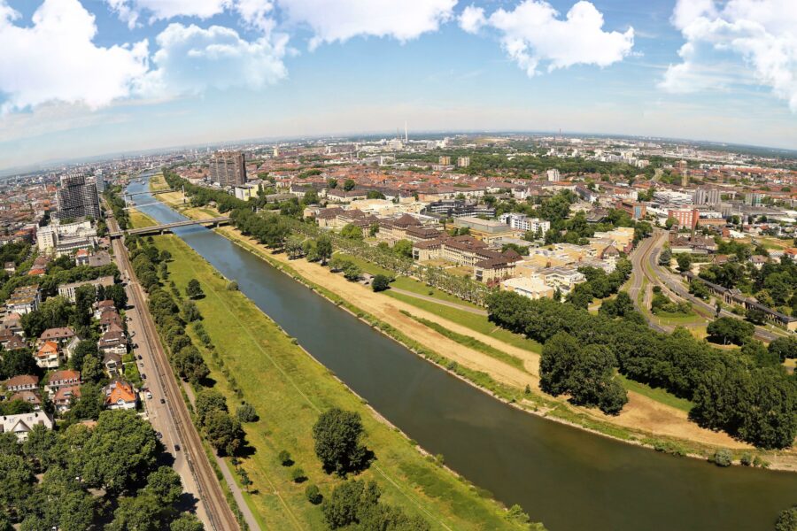 Fluss mit grünen Uferstreifen, Brücken und städtischer Landschaft im Hintergrund.