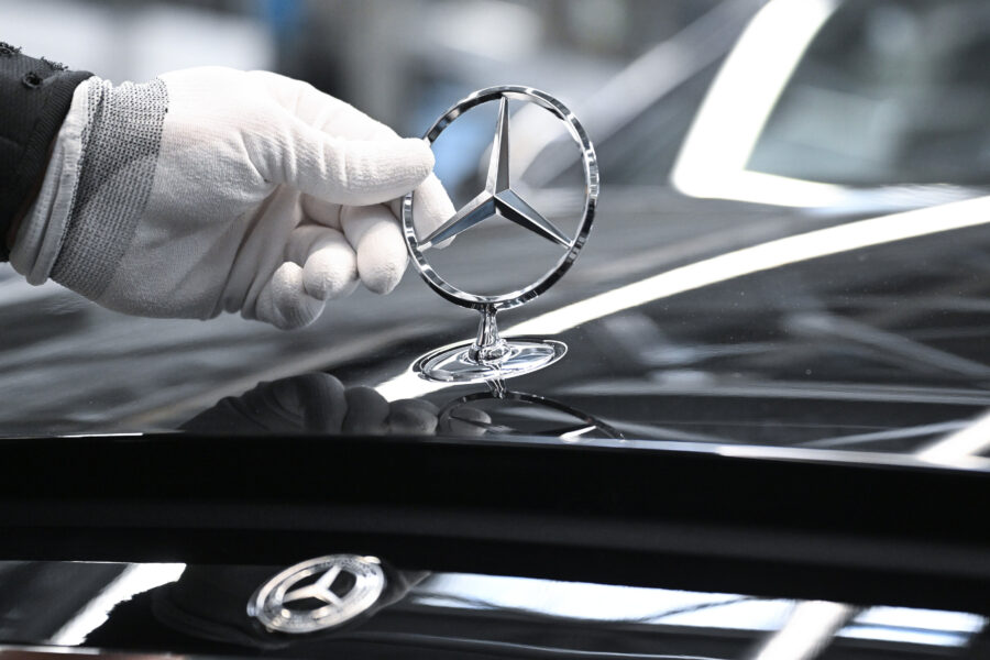 Hand mit Handschuh hält ein Mercedes-Emblem auf einer glänzenden Motorhaube.