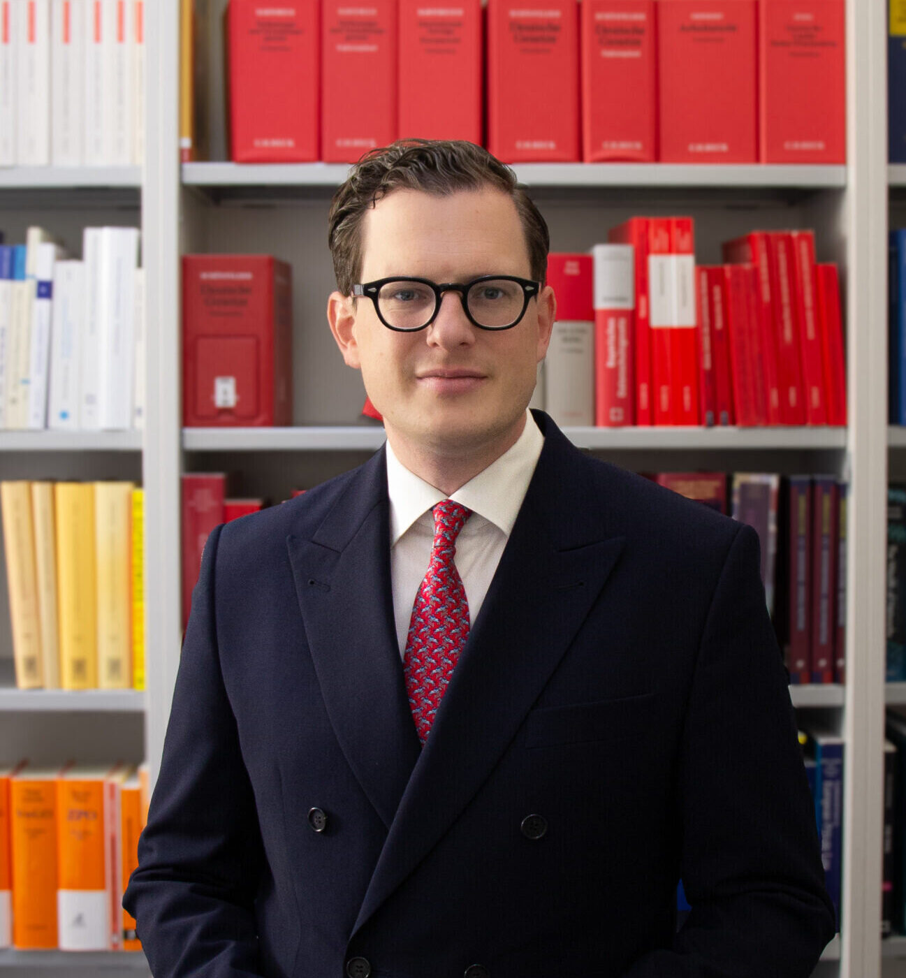 Mann in Anzug vor Bücherregal mit roten und weißen Büchern.