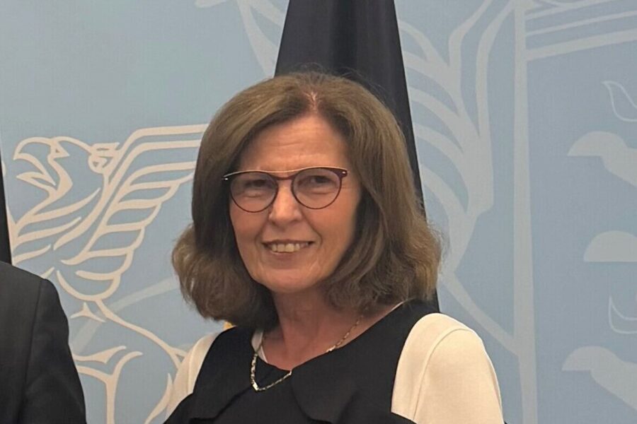 Eine lächelnde Frau mit Brille vor blauem Hintergrund mit Adlermotiv.