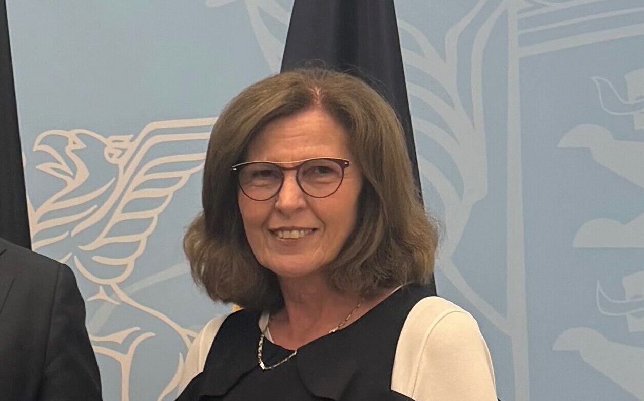 Eine lächelnde Frau mit Brille vor blauem Hintergrund mit Adlermotiv.