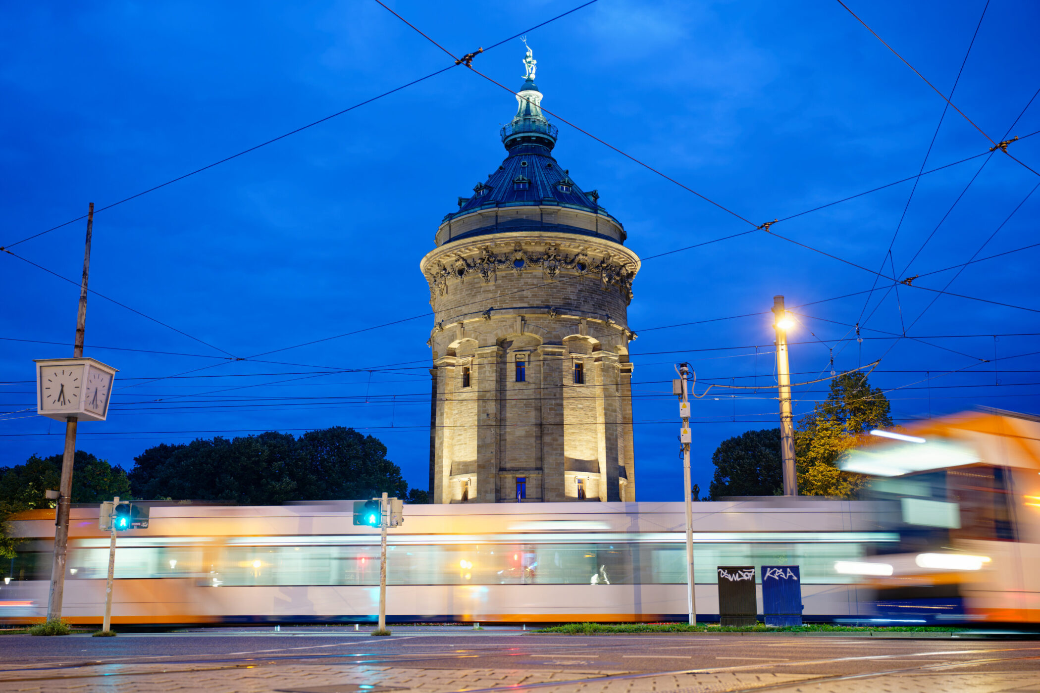 Turm bei Nacht, Straßenbahn vorbei, Uhr zeigt 9:50, Bäume im Hintergrund.