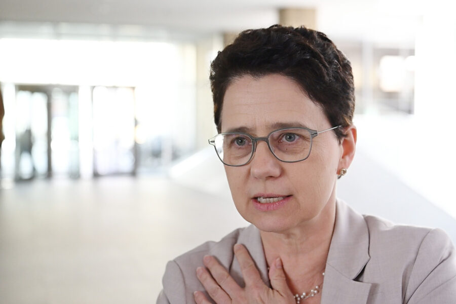 Frau mit Brille und kurzem Haar in einem hellen Raum.