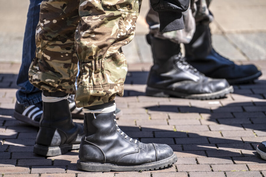 Schwarze Stiefel und Tarnhosen auf Pflastersteinen.