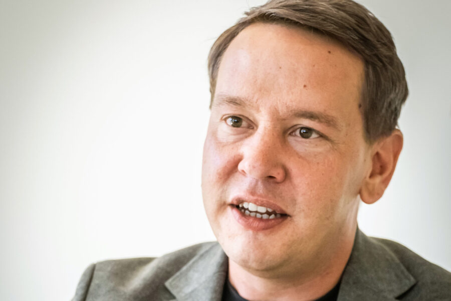 Ein Mann in grauem Sakko spricht mit offenem Mund.