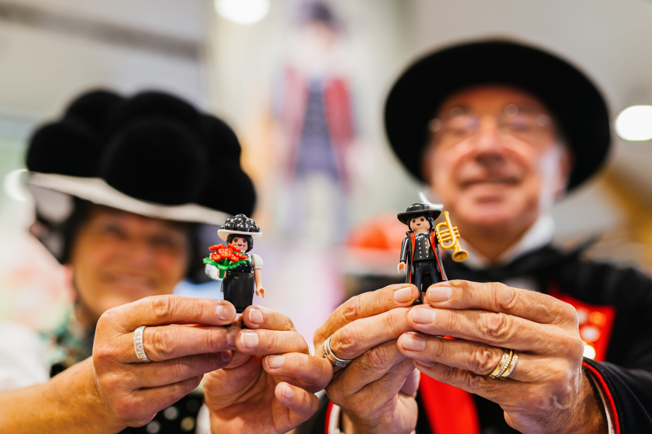 Zwei Menschen halten Playmobilfiguren im Bollenhut und Tracht.