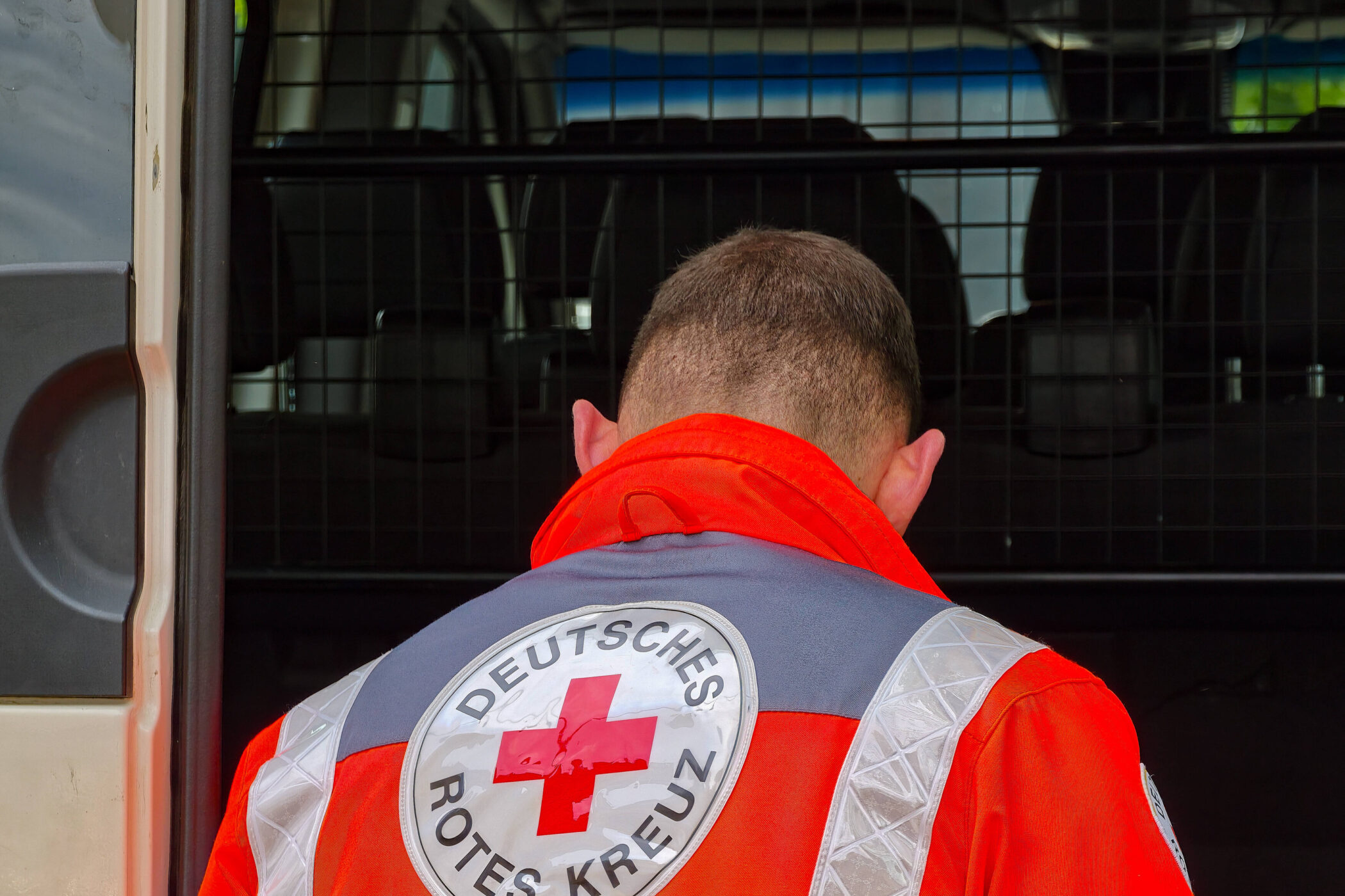 Person in roter Jacke mit "Deutsches Rotes Kreuz"-Aufschrift vor Fahrzeug.