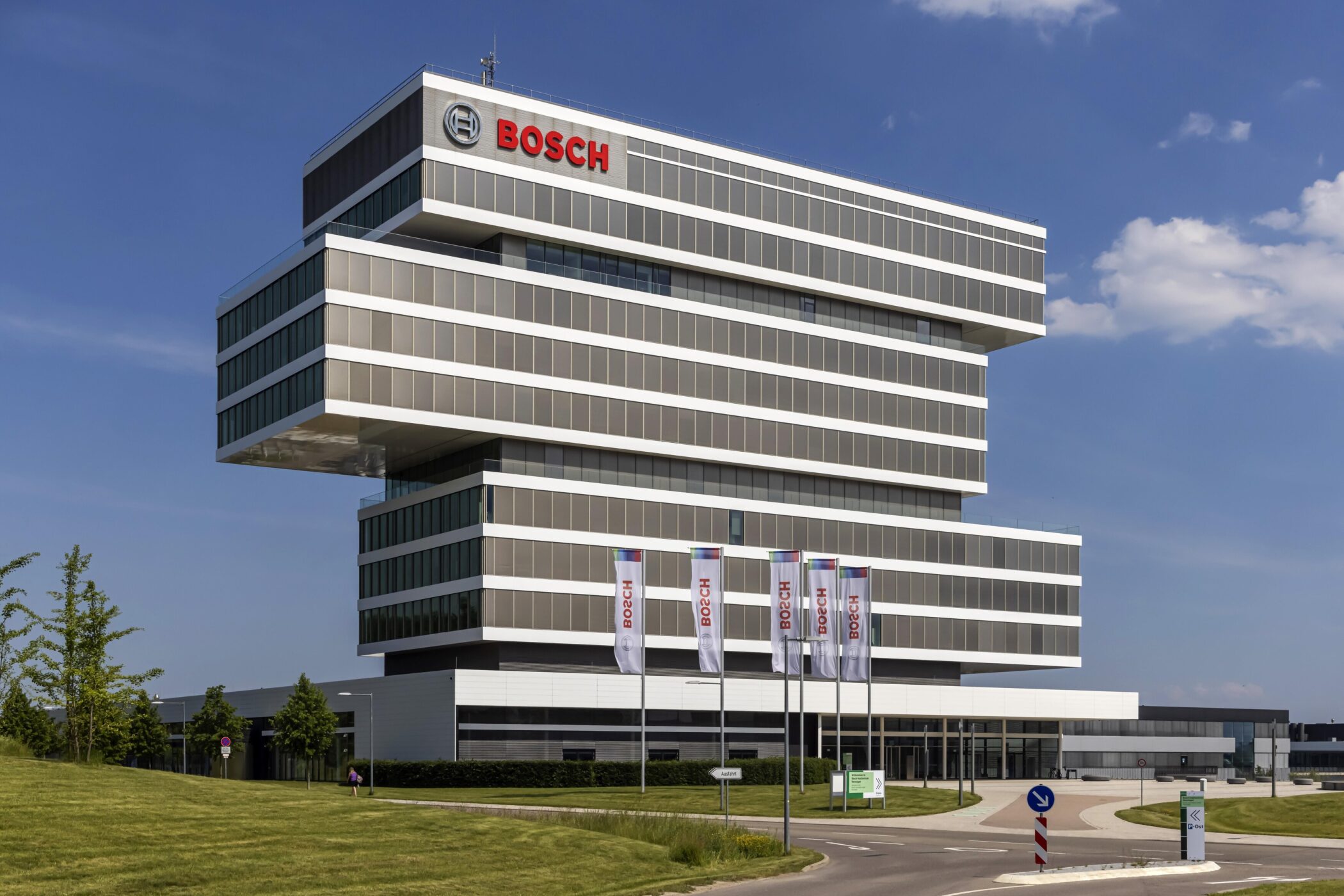 Modernes Gebäude mit "Bosch"-Logo und Fahnen davor, blauer Himmel im Hintergrund.