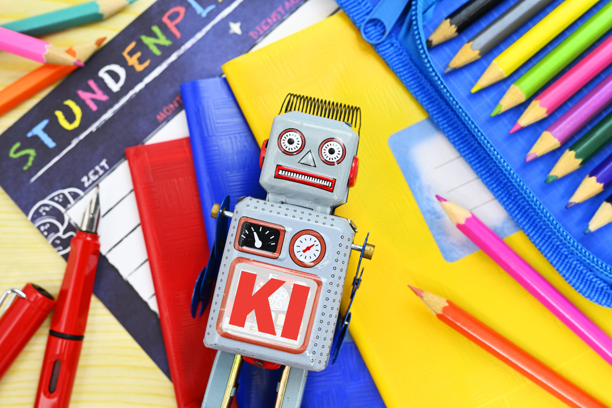 Bunter Stundenplan, Bleistifte, Roboter mit "KI" auf der Brust, rote Stifte, Hefte.