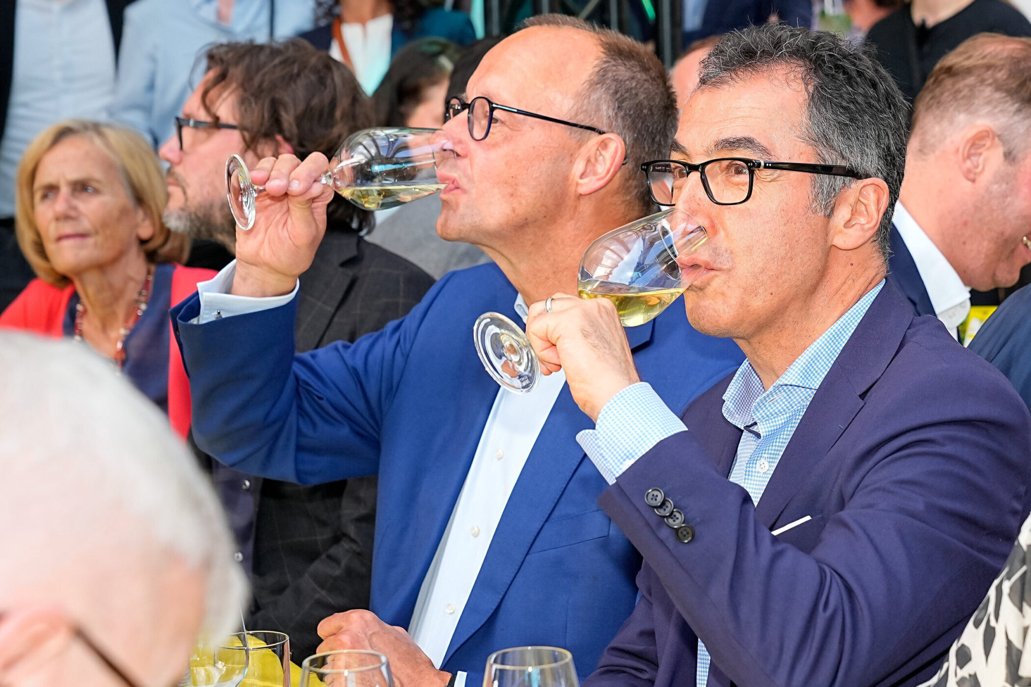 Menschen bei einer Veranstaltung trinken Weißwein aus Weingläsern.