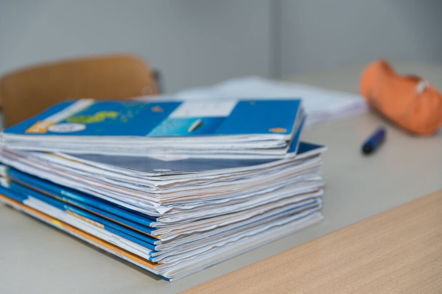 Ein Stapel blaue Ordner auf einem Tisch neben einem orangefarbenen Mäppchen.
