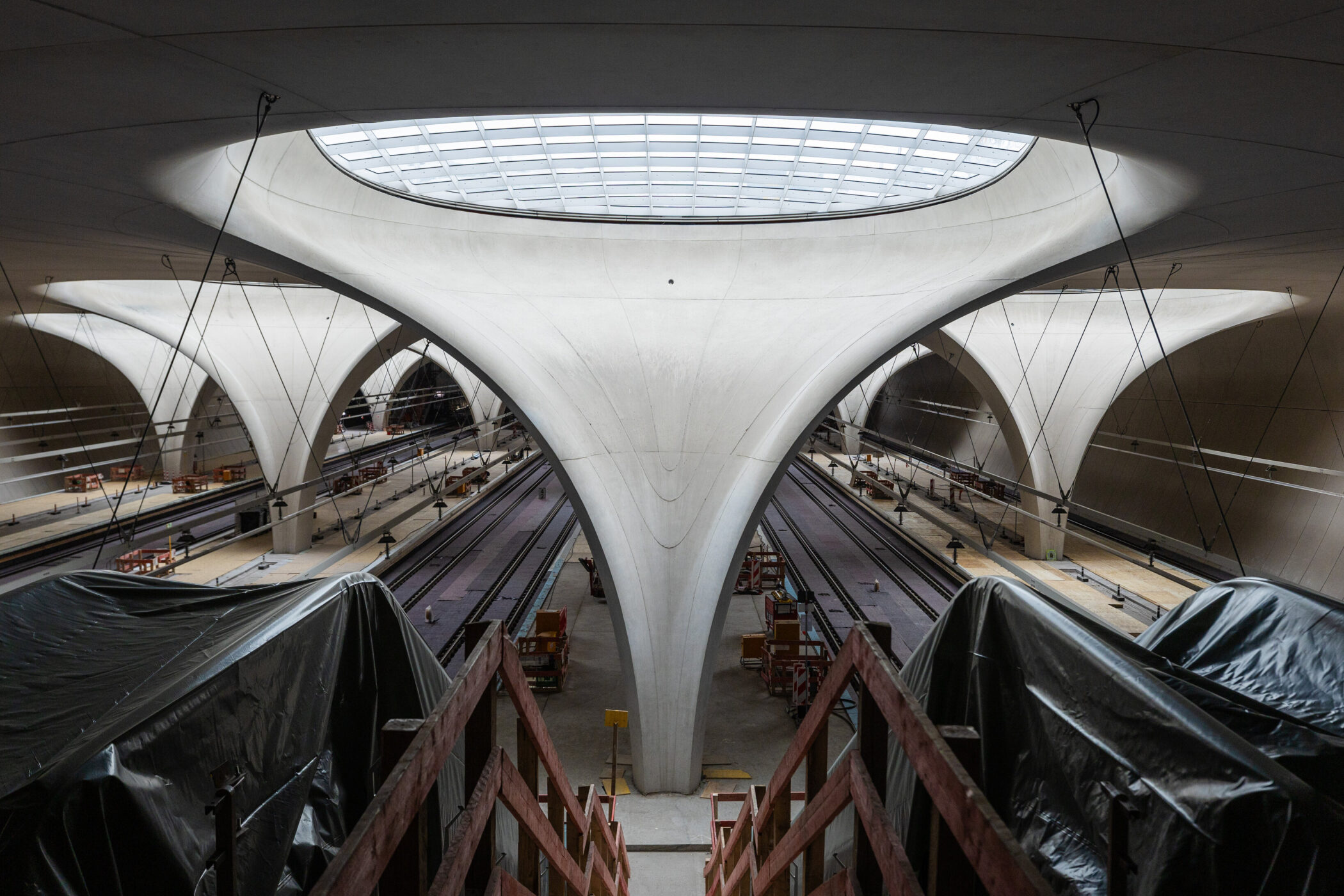 Moderne Halle mit mehreren Gleisen, geschwungene Dachstruktur, beleuchtet von Oberlicht.