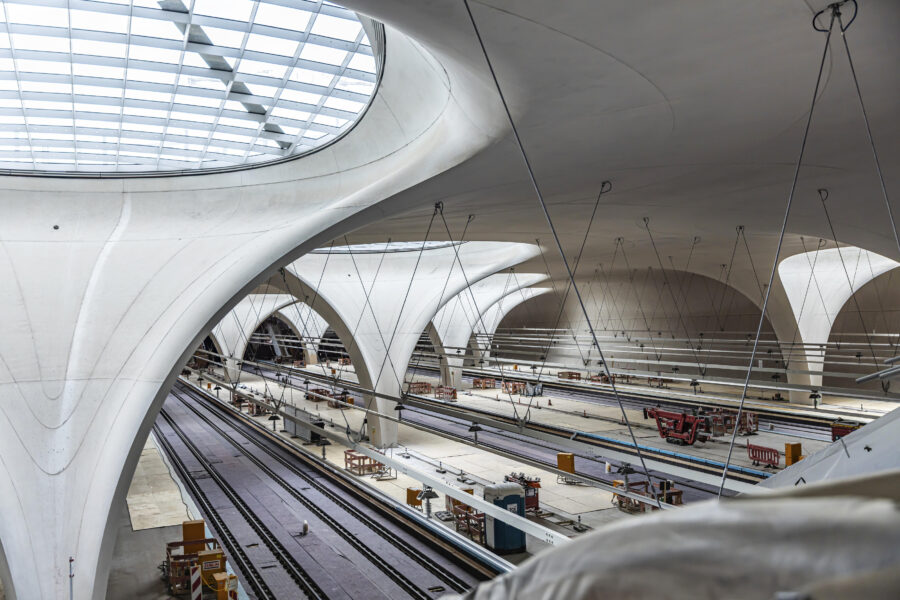 Großer, heller Bahnhof mit modernen Betonbögen und leeren Bahngleisen.