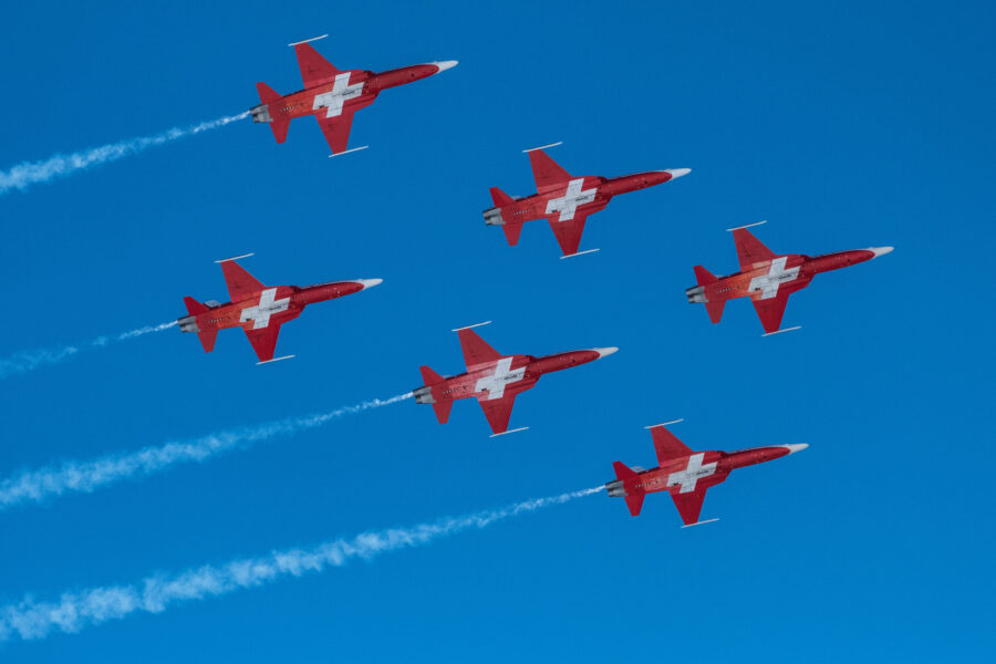 Sechs rote Flugzeuge mit weißen Kreuzen fliegen in Formation am blauen Himmel.