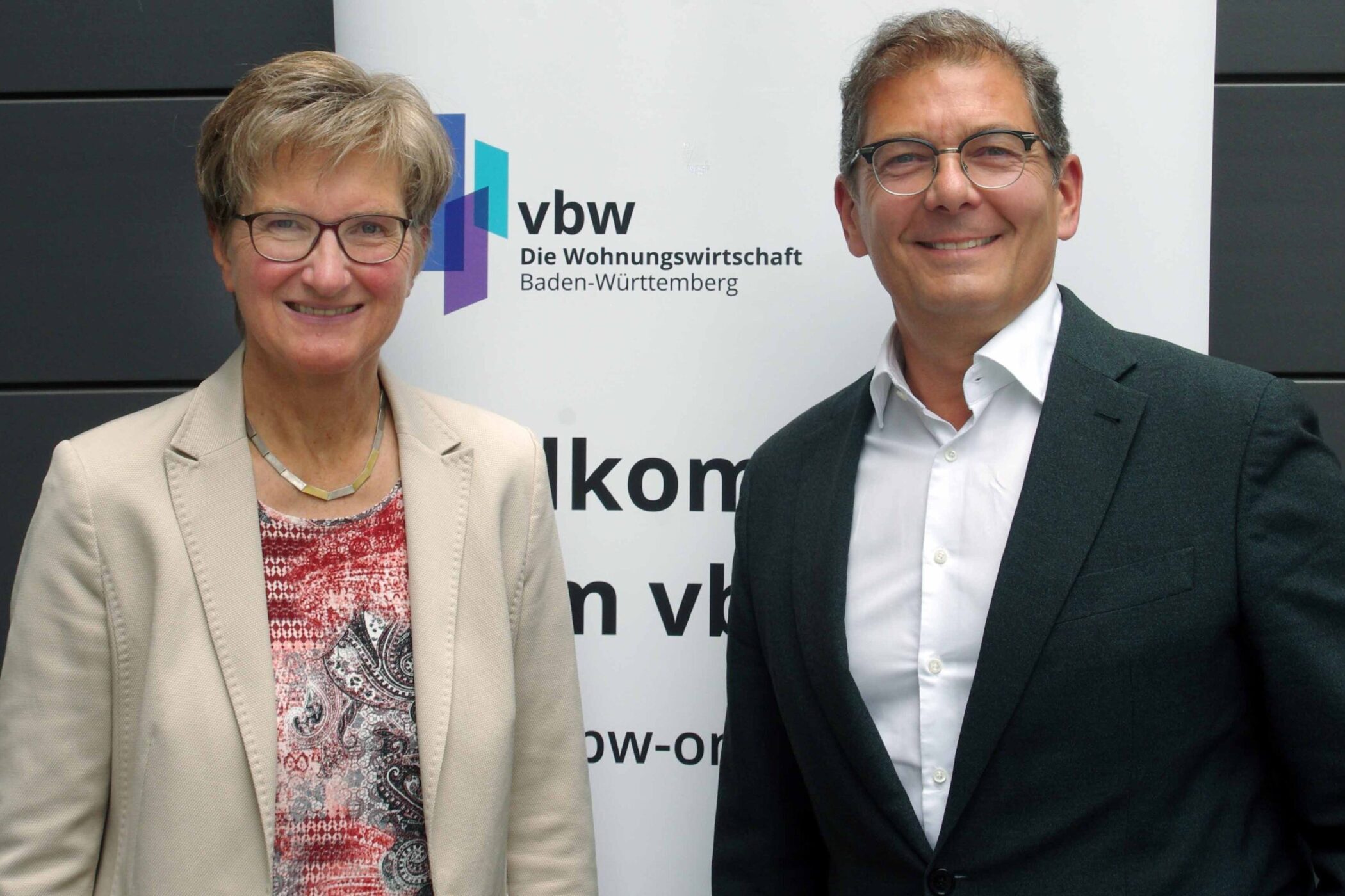 Zwei Personen vor einem Banner mit der Aufschrift „vbw Wohnungswirtschaft“.