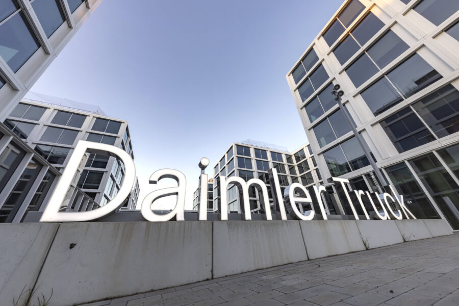 Große Leuchtschrift „Daimler Truck“ vor modernen Bürogebäuden.