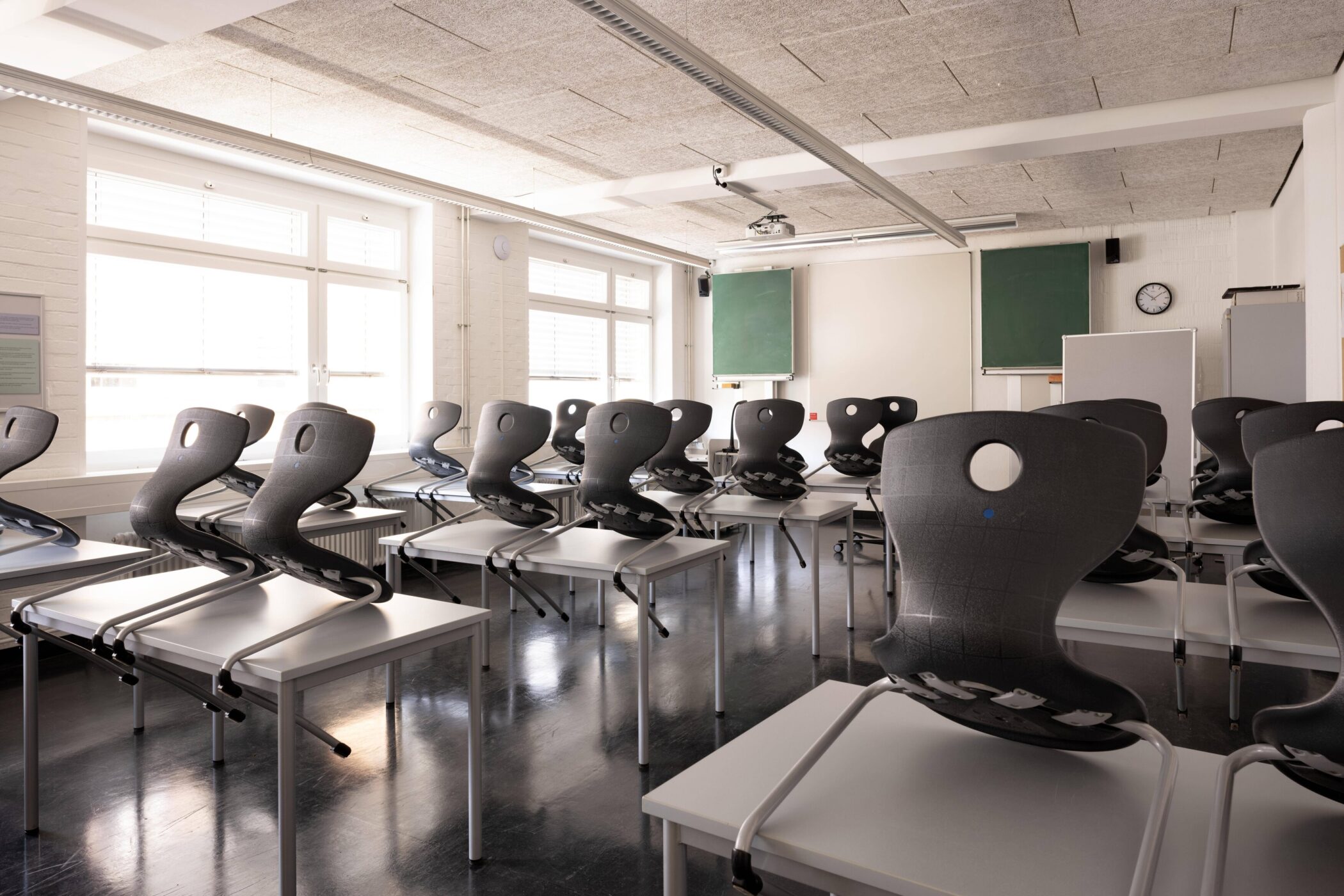 Leerer Klassenraum mit Stühlen auf Tischen, Tafel und Uhr an der Wand.