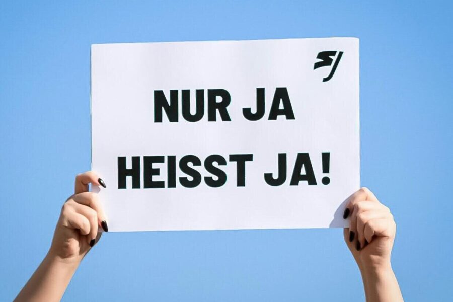 Zwei Hände halten ein Schild mit der Aufschrift "NUR JA HEISST JA!" vor blauem Himmel.