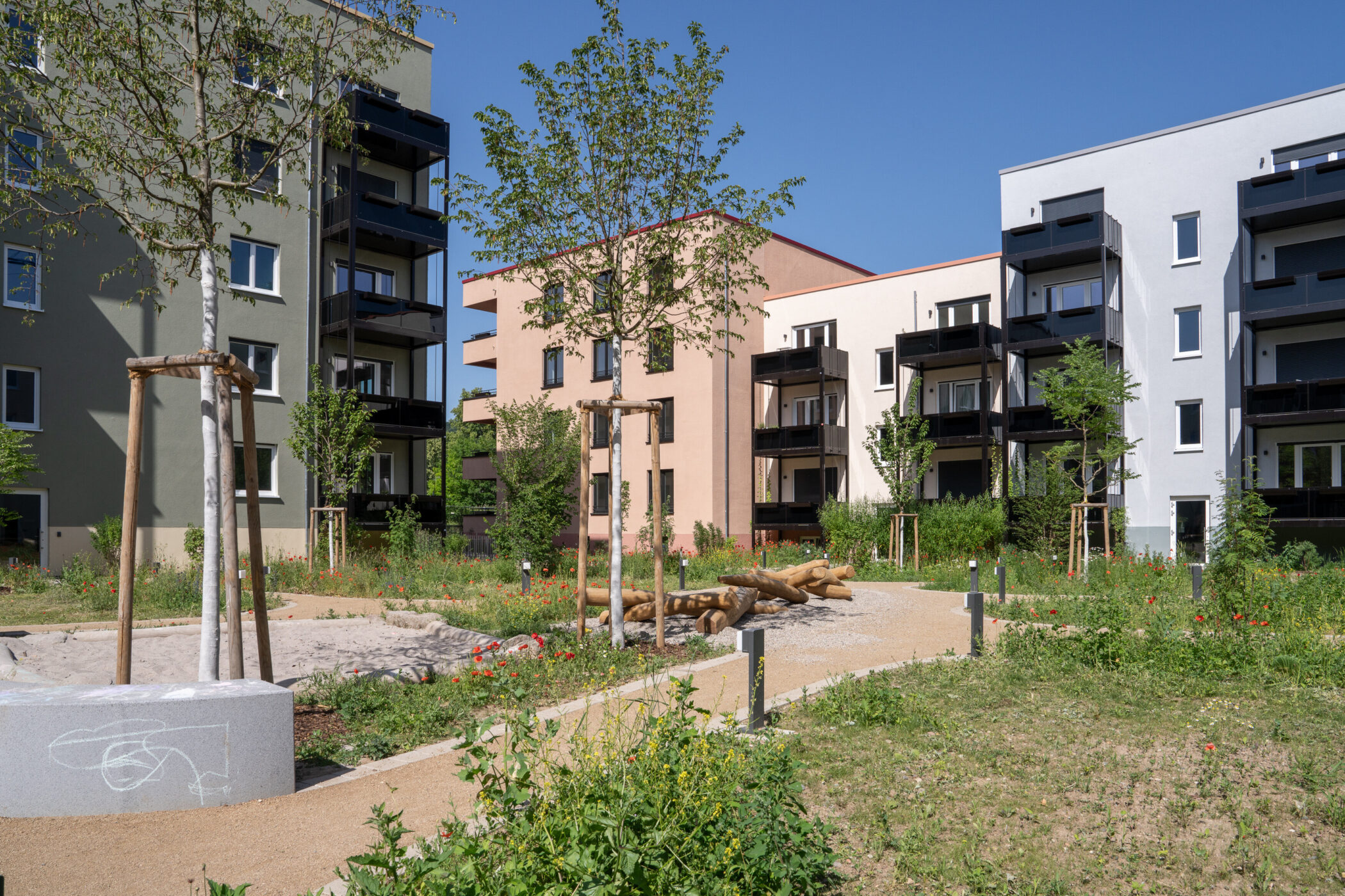 Mehrstöckige Wohngebäude, Garten mit Bäumen und Holzspielgerüst im Vordergrund.