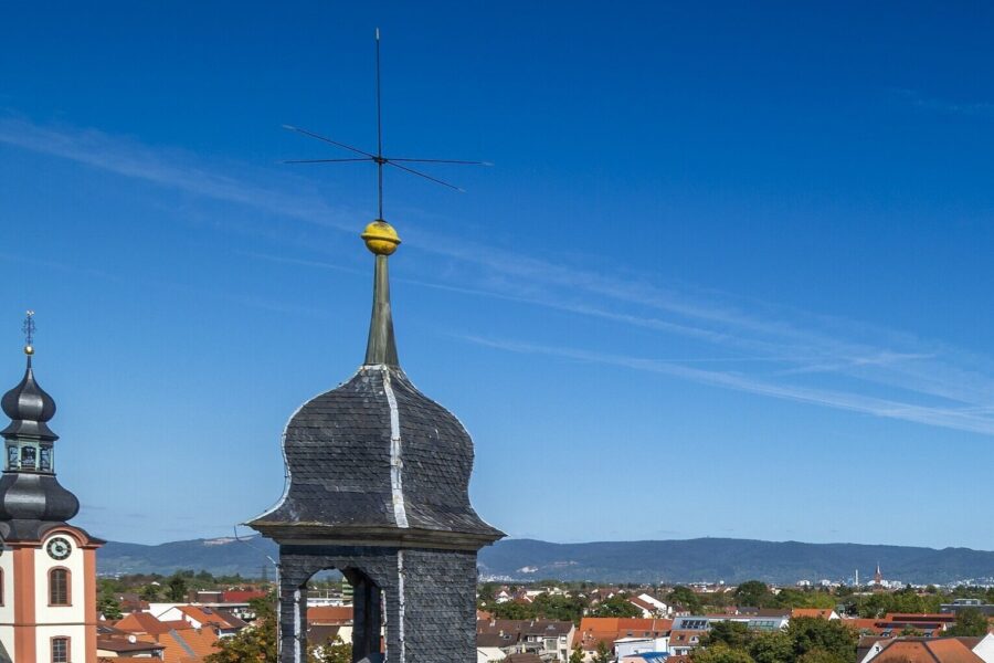 Zwei Kirchturmspitzen mit Antennen vor blauem Himmel.