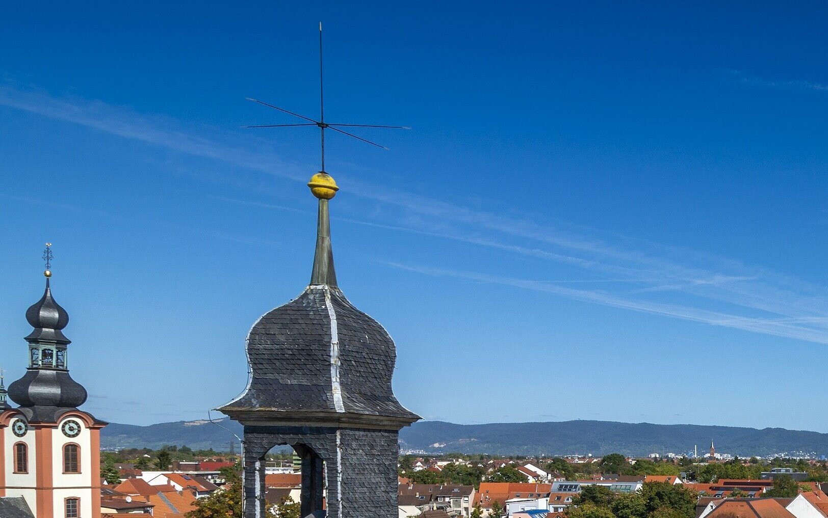 Zwei Kirchturmspitzen mit Antennen vor blauem Himmel.