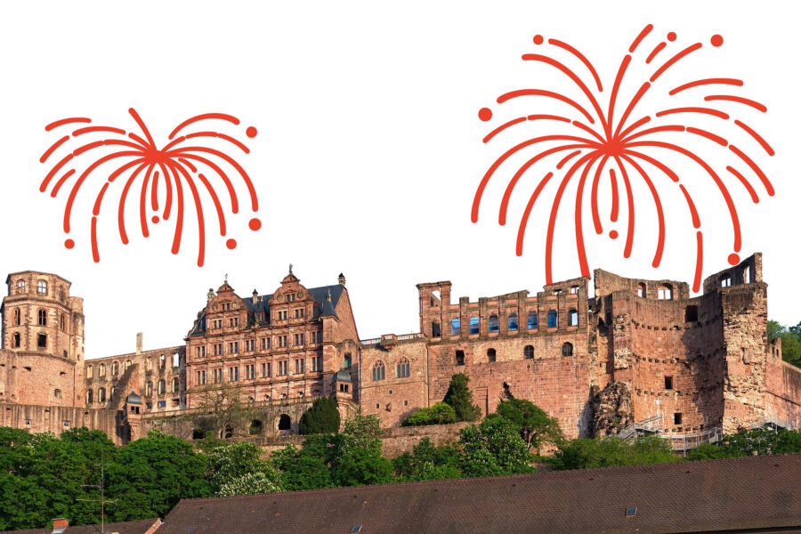 Burg mit rotem Feuerwerk im Hintergrund, grüne Vegetation im Vordergrund.