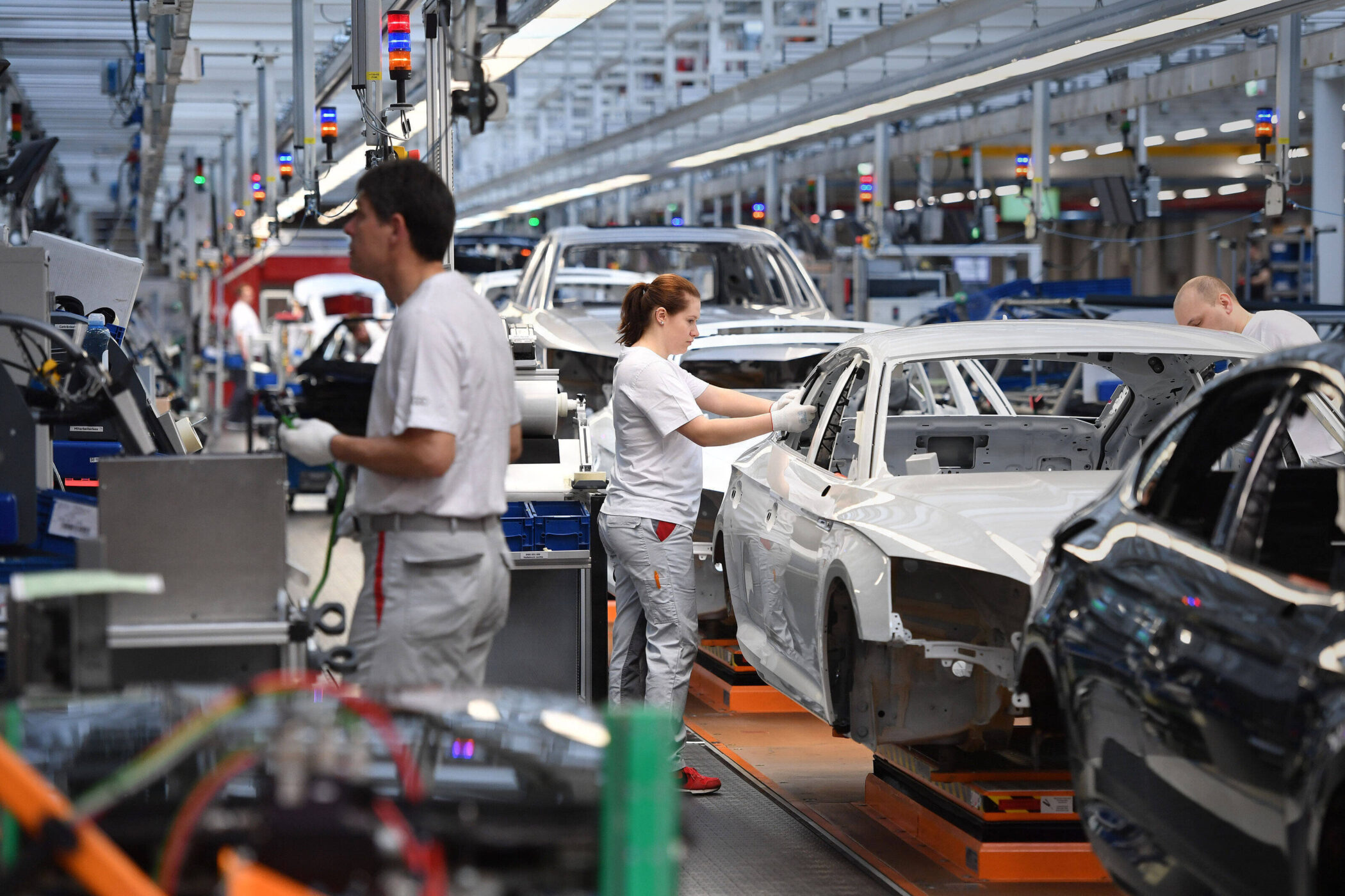 Drei Personen arbeiten in einer Autoproduktion, Karosserien in Linie.