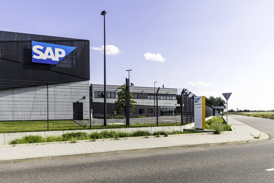 Gebäude mit SAP-Logo, umzäunt, davor Straße und Gehweg.