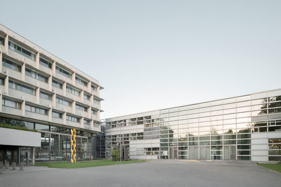 Modernes Gebäude mit Glasfassade und gelber Skulptur, Aufschrift "Neubau 2".