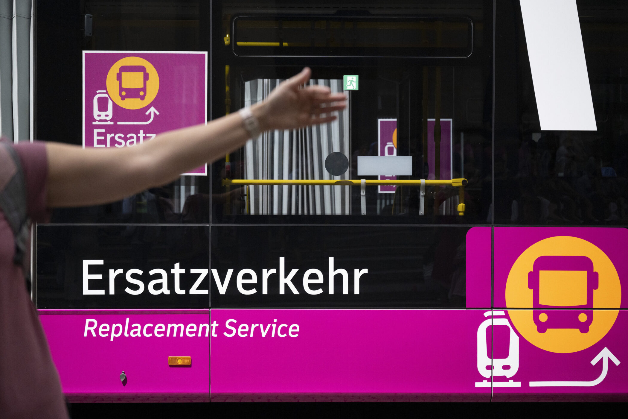 Bus mit "Ersatzverkehr" Beschriftung, erhobener Arm im Vordergrund.
