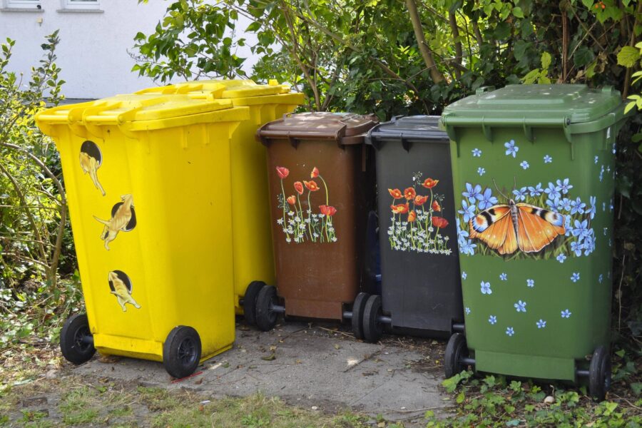 Vier bunte Mülltonnen mit Tier- und Blumenmotiven in einer Reihe.